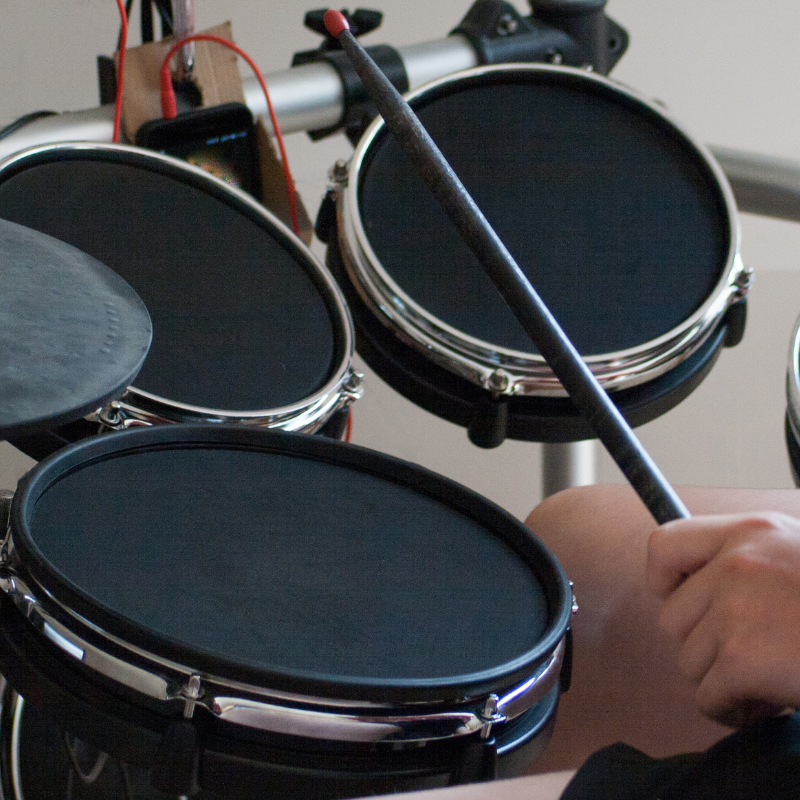 Close-up of a person playing electronic drums with drumsticks.