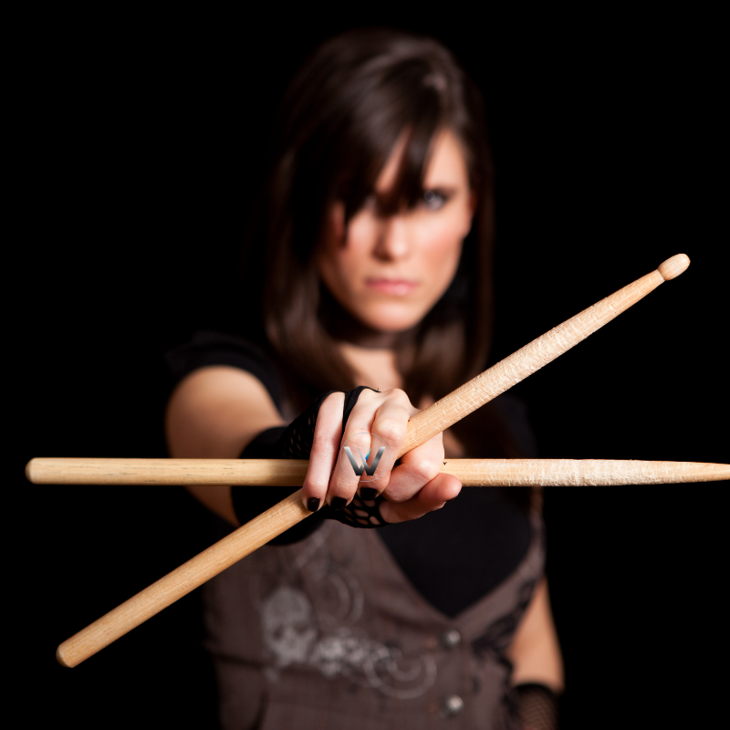 Woman holding drumsticks against a black background