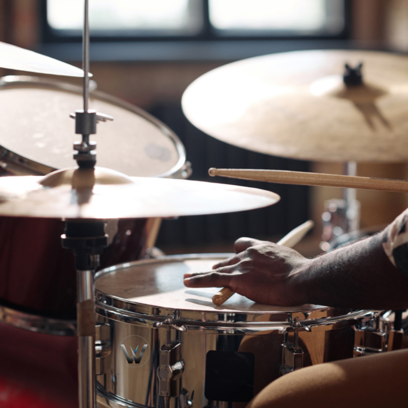 Close-up of a person playing drums with a focus on the snare drum and cymbals.