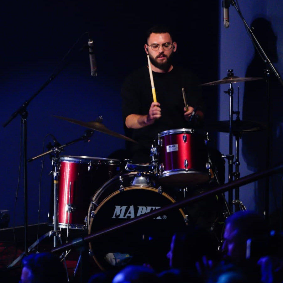 Man playing drums on a stage with a blue background